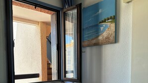 Quarto com cama, mesa de cabeceira com abajur, janela com cortinas e um quadro na parede.