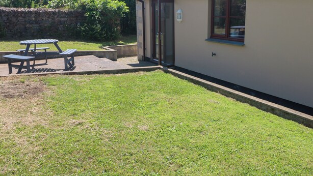 Un edificio con pared de piedra, jardín con césped y zona de mesas de picnic.