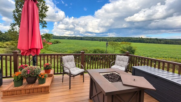 A wooden deck with two chairs, a table, and a red umbrella.