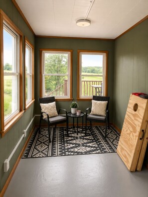 Une pièce avec deux chaises, une petite table et une vue sur une terrasse en bois, visible à travers de grandes fenêtres.