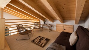 A cozy loft bedroom with a sloped ceiling, wooden beams, a sofa, two wicker chairs, a small table, and a cabinet.