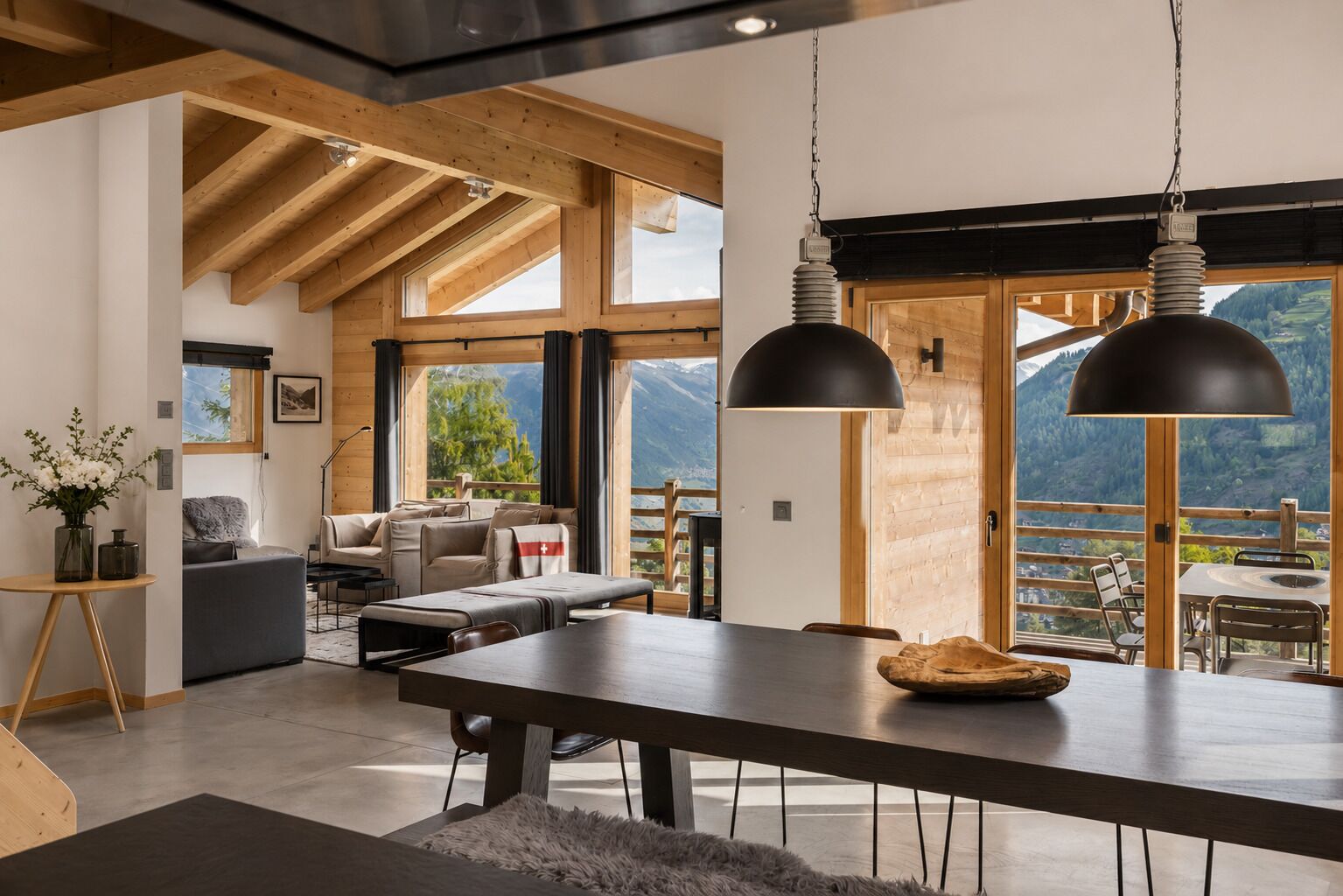Ein modernes Interieur mit Essbereich, Holzbalken, großen Fenstern und Bergblick.