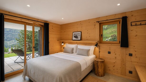 A bedroom with a bed, a window, a chair, and a view of the outdoors.