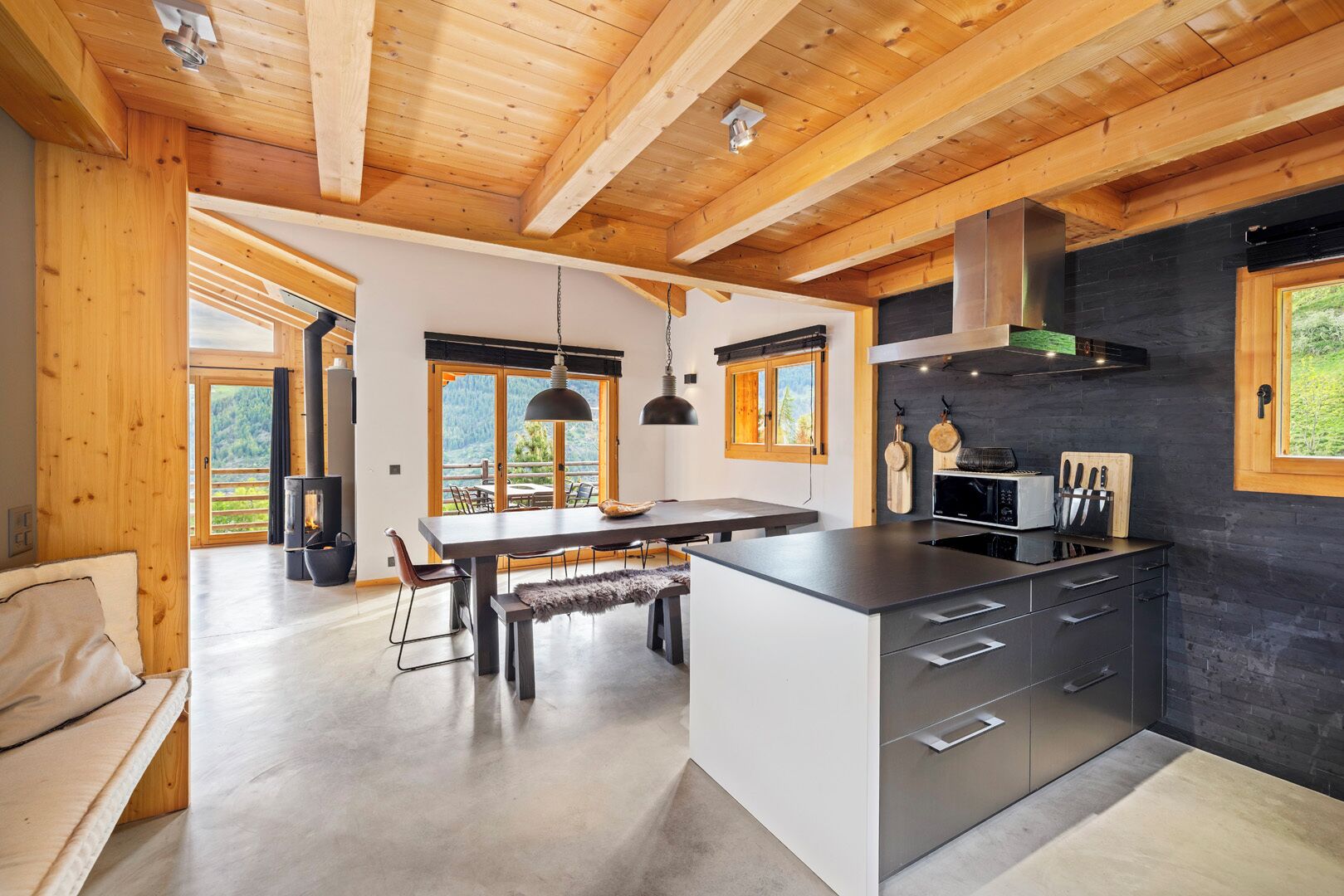 A modern kitchen with a central island, wooden beams, and a view of the outdoors.