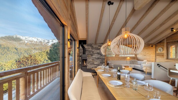 A dining area with a wooden table set for a meal, a fireplace, and a view of a mountainous landscape. - Chalet Montâme - Modern Luxury in the Swiss Alps (Riddes)