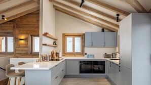 A modern kitchen with a central island, built-in appliances, and wooden beams on the ceiling. - Chalet Montâme - Modern Luxury in the Swiss Alps (Riddes)