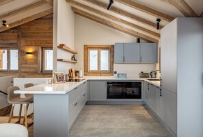 Eine moderne Küche mit einer zentralen Kochinsel, integrierten Geräten und Holzbalken an der Decke.