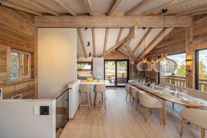 Eine moderne Küche mit Holzbalken, einem Essbereich mit großem Tisch und Blick ins Freie.