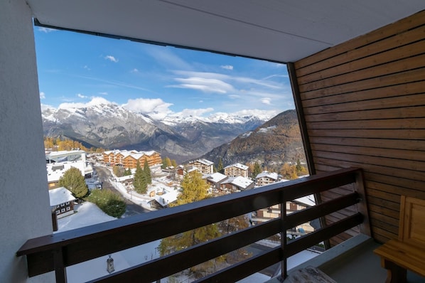 Varanda com vista para um resort na montanha, corrimão de madeira e edifícios cobertos de neve.
