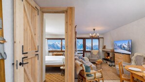 A cozy room with a bed, sofa, and dining area, featuring a fireplace and a TV. - Apartment Mont-parrain C28 Cosy & Central With Private Parking (Riddes)