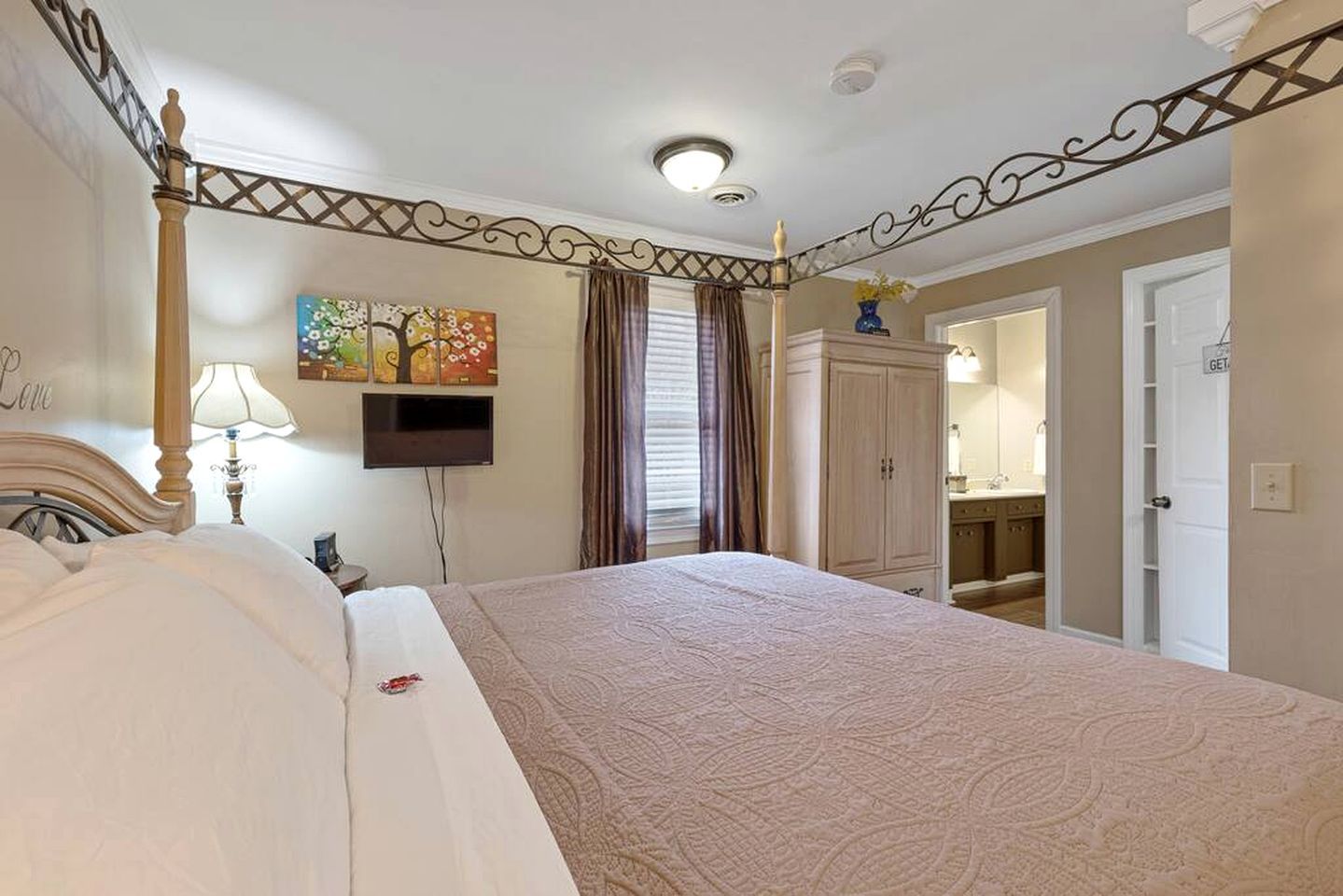 Habitación de hotel con cama, televisión, armario y baño visible a través de una puerta abierta.