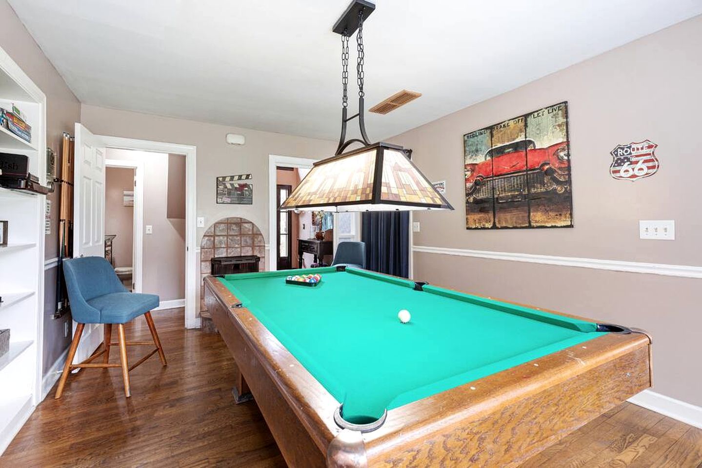A pool table with a hanging lamp, a blue chair, and a billiards rack.