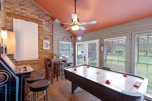 A pool table with stools, a bar area, and a ceiling fan in a room with large windows.
