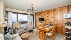 A cozy living room with a dining area, wooden walls, a TV, and a view of the mountains. - Apartment Mont-parrain C32 Bright & Central With Balcony (Riddes)