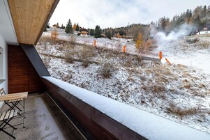 A view from a window overlooking a snowy landscape with a train passing by, a wooden staircase, and a bench.