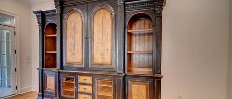 Suuri, tumma puinen kirjahylly, jossa on useita hyllyjä ja laatikoita, sijaitsee huoneessa, jossa on parkettilattia ja valkoiset seinät.