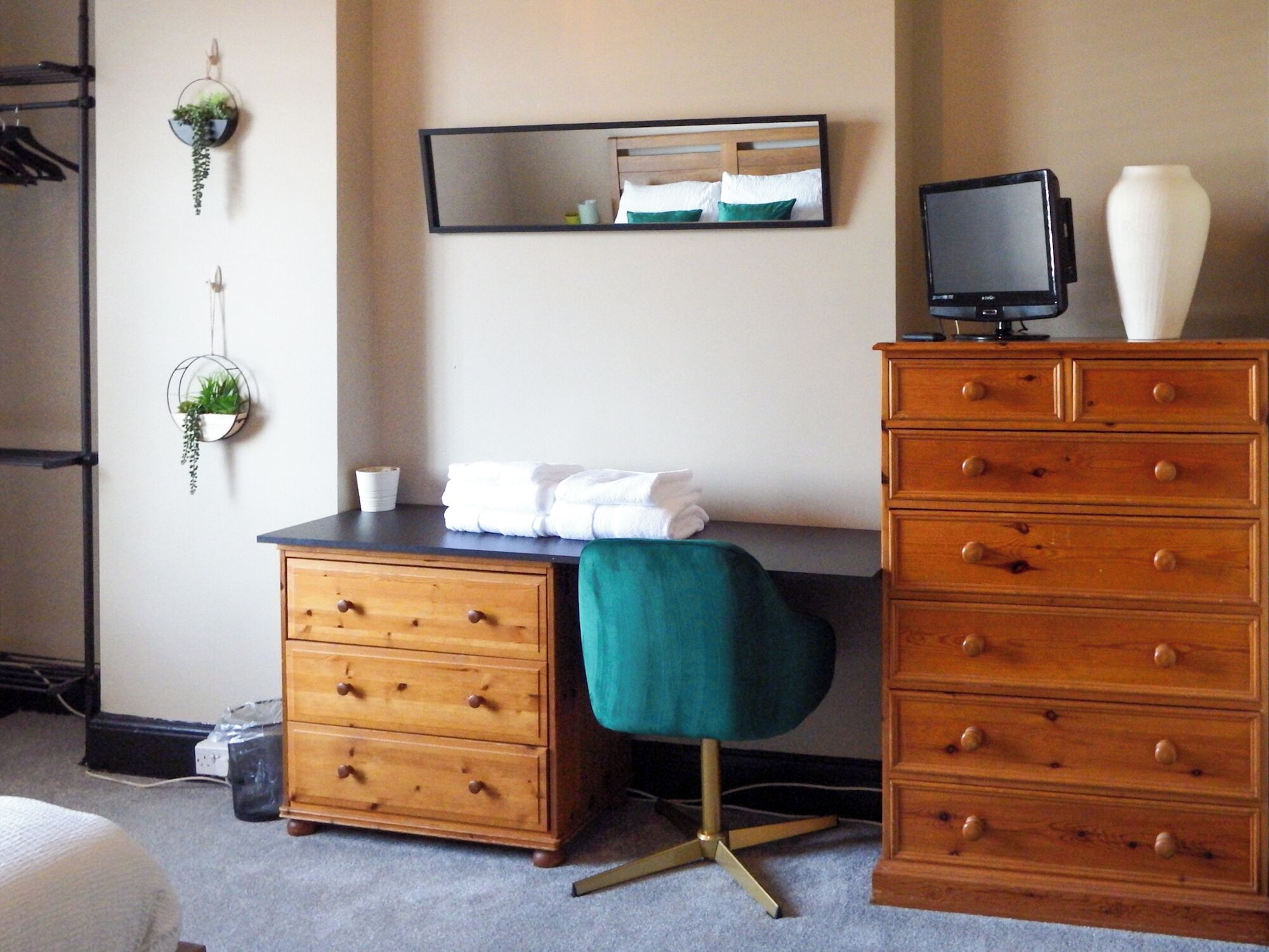 A hotel room with a bed, a dresser, a desk, a chair, a mirror, a television, and two wall-mounted planters.