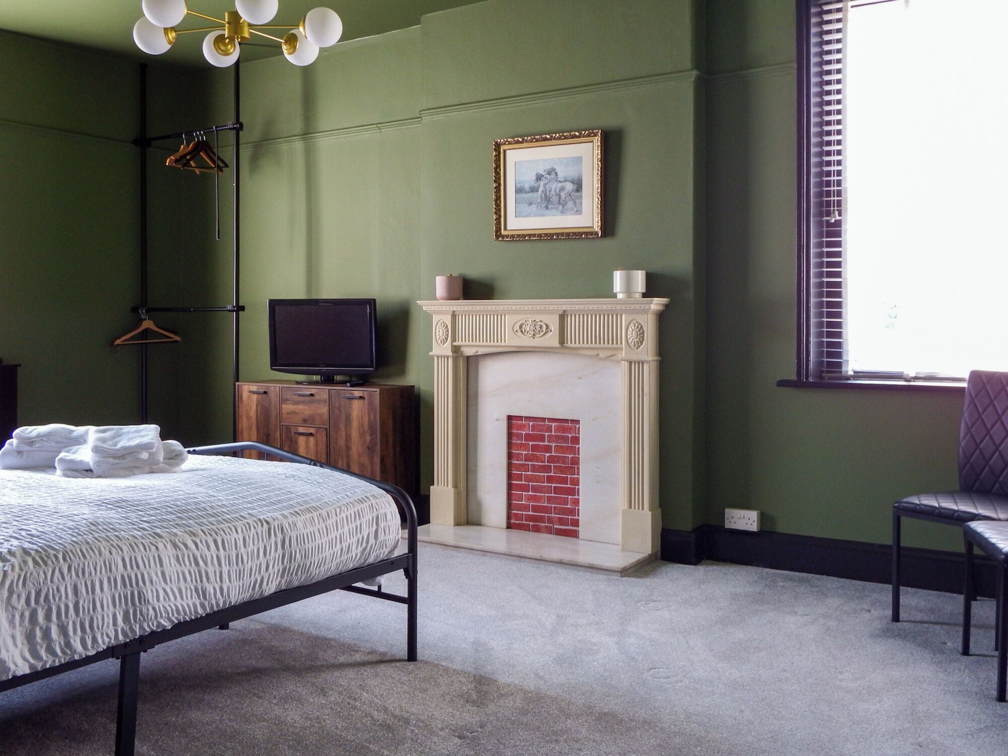 Ein Schlafzimmer mit einem Bett, einem Fernseher auf einer Holzkommode, einem Kamin und einem Fenster mit Jalousien.