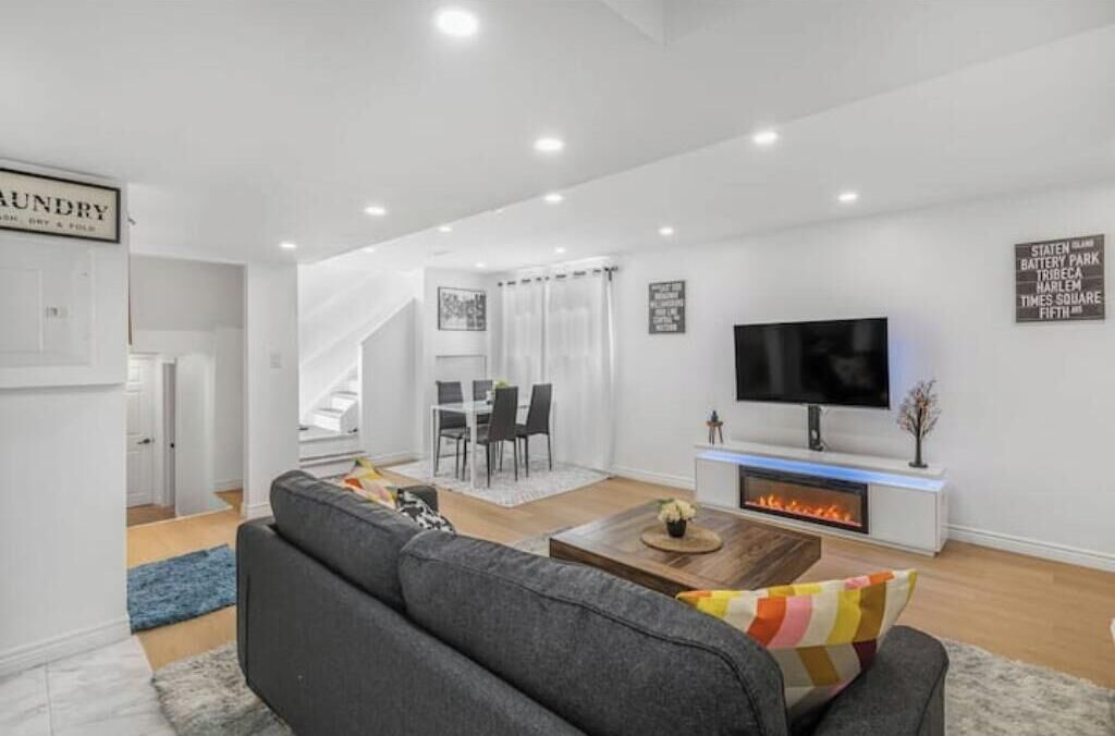A modern living room with a fireplace, a television, and a dining area with a staircase.