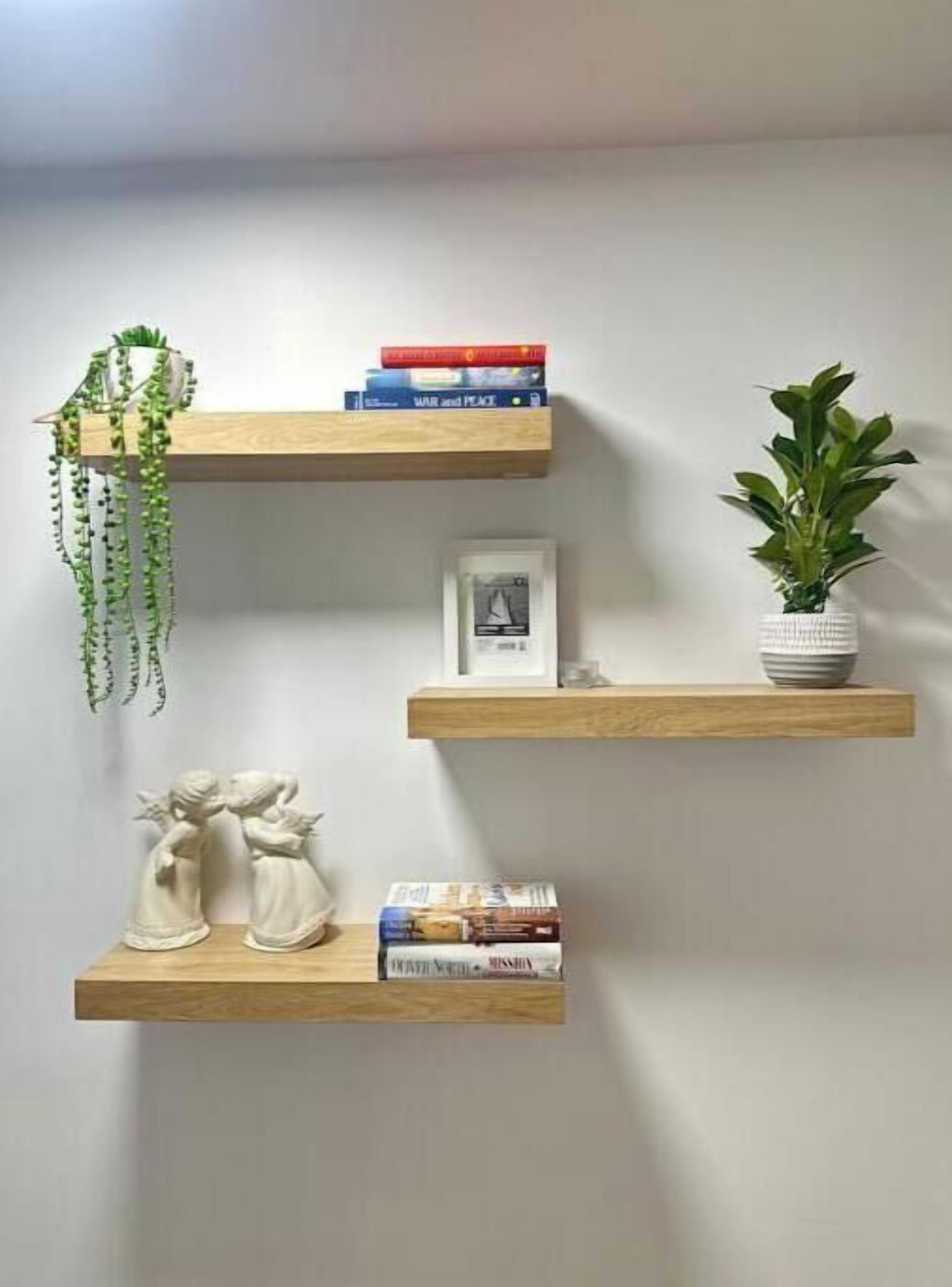 Three wooden shelves against a wall, each holding books, a framed picture, and a plant.