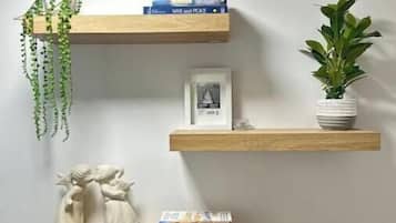 Three wooden shelves against a wall, each holding books, a framed picture, and a plant.