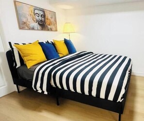 A bed with a black frame, a striped bedspread, and multiple pillows in yellow and blue. - Cozy Niagara Retreat with Fireplace (Thorold)