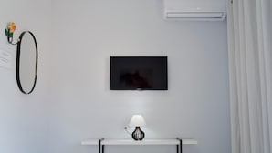Una habitación con televisión instalada, aire acondicionado de pared y una pequeña mesa con lámpara.