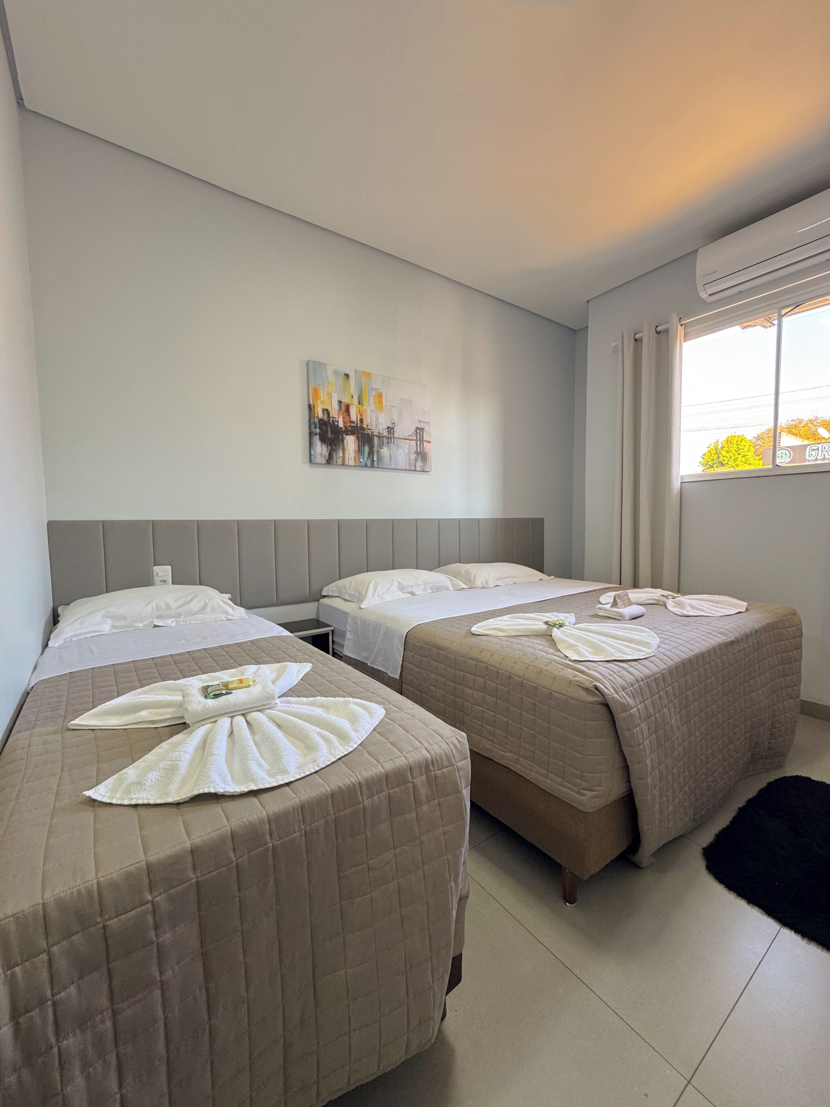 A hotel room with two beds, a painting on the wall, and an air conditioning unit.