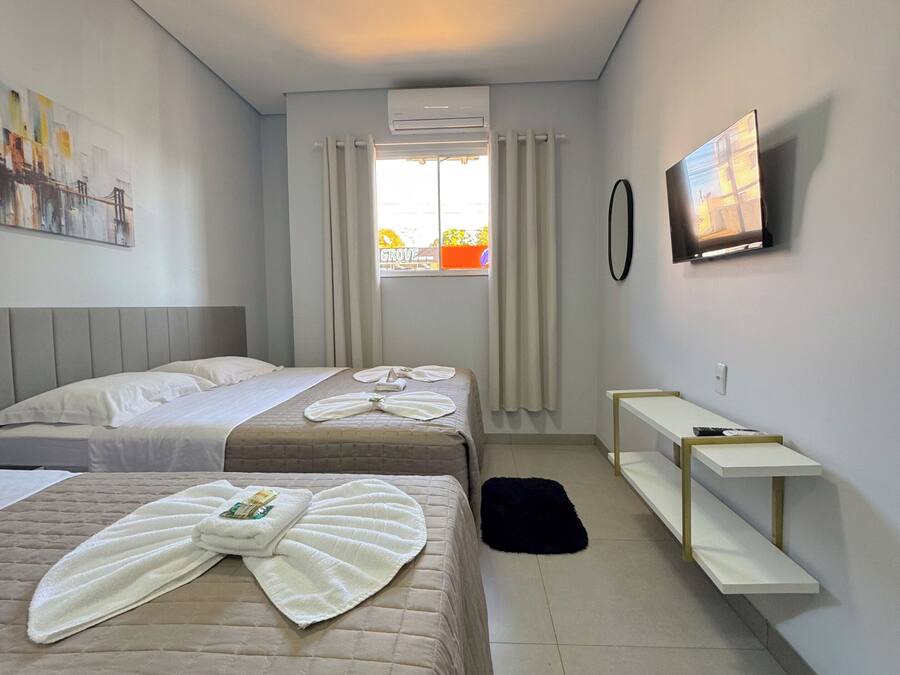 Habitación de hotel con dos camas, un televisor, un equipo de aire acondicionado, un cuadro en la pared y una ventana con cortinas.