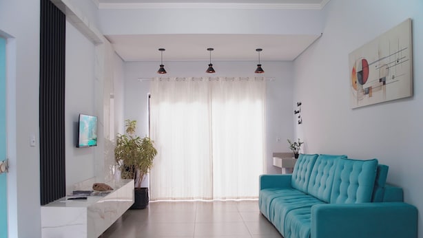 Una sala de estar moderna con un sofá color turquesa, una chimenea de mármol y un ventanal con cortinas translúcidas.