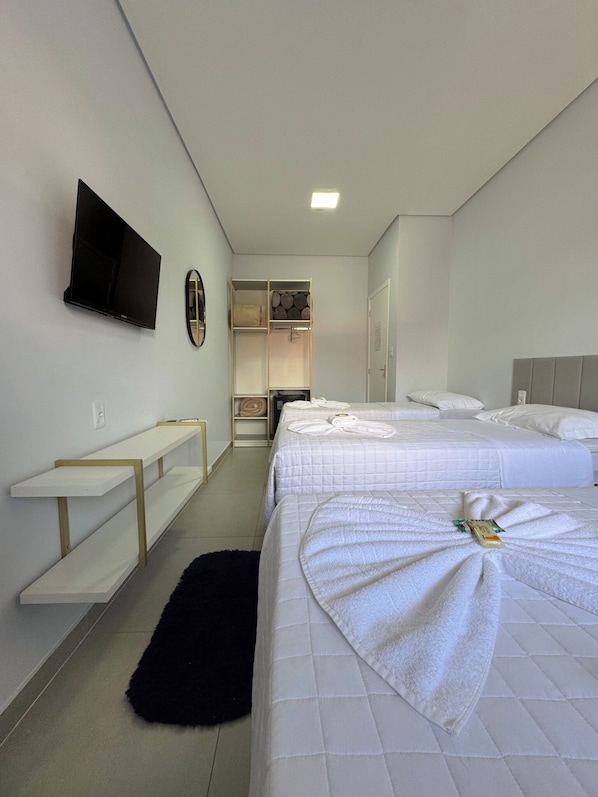 Quarto de hotel com duas camas, televisão de tela plana, espelho, guarda-roupa e uma mesa pequena.