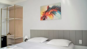 Una habitación de hotel con cama, armario, un cuadro y mesita de noche.