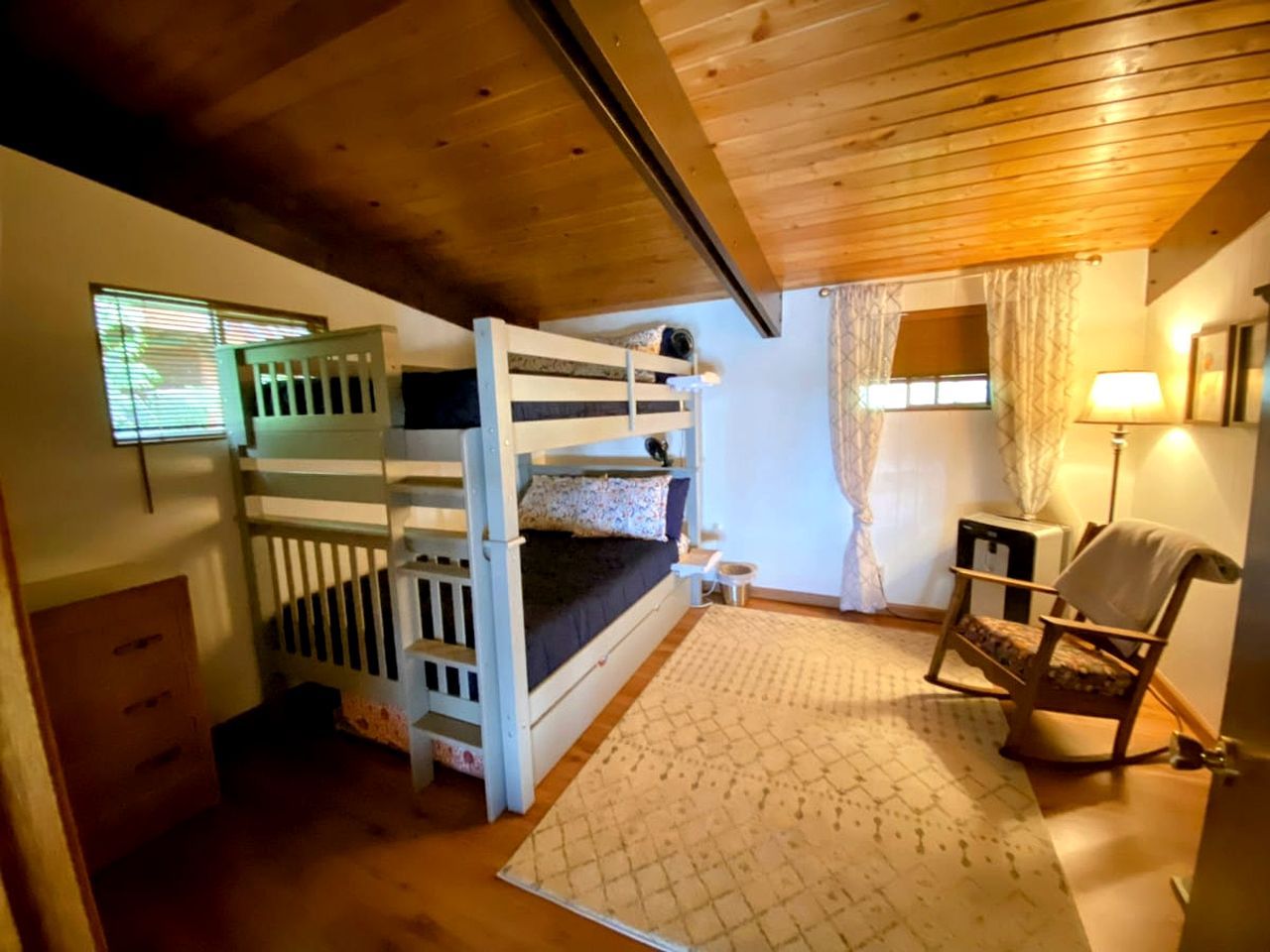 Une chambre avec des lits superposés, une chaise, une lampe et une petite table.