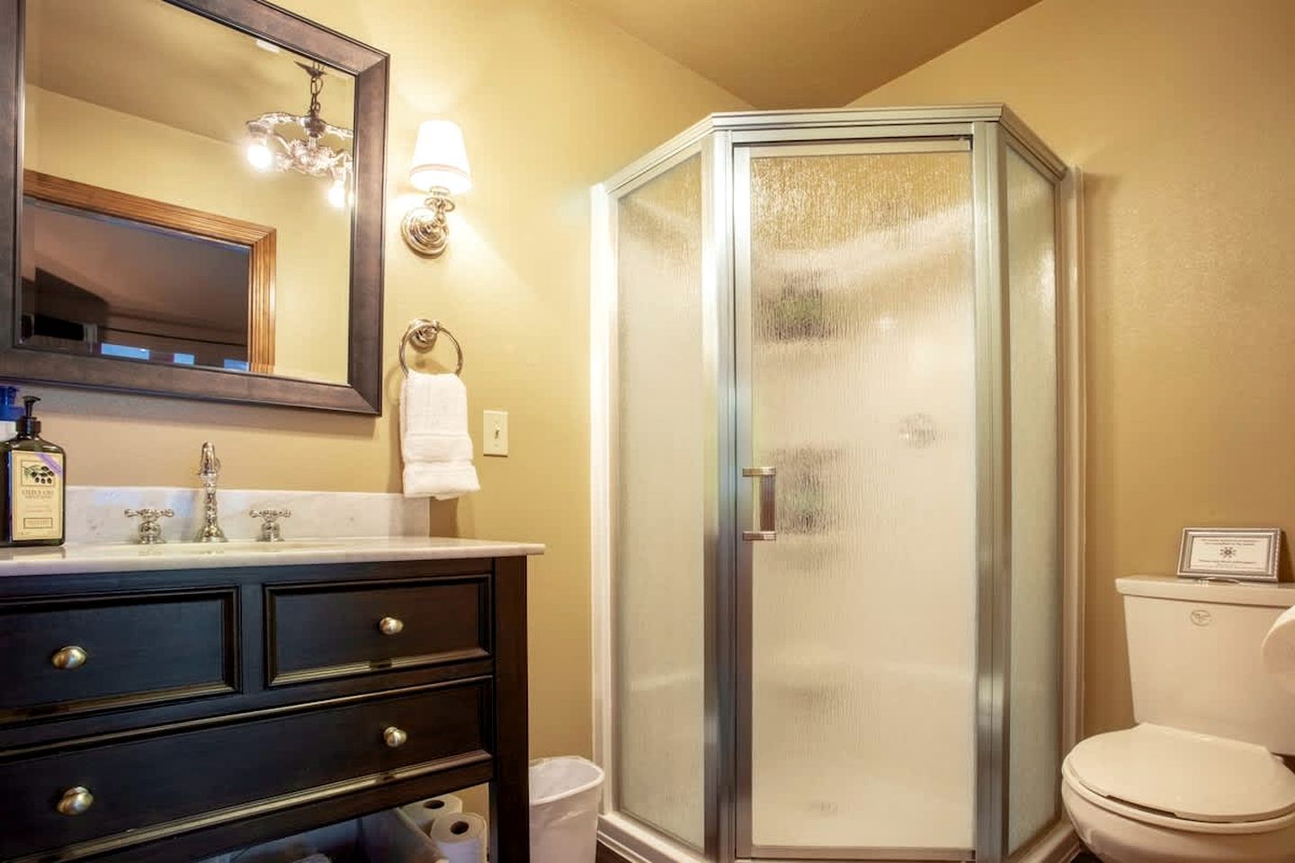 A bathroom with a dark vanity, a mirror, a glass shower enclosure, and a toilet.