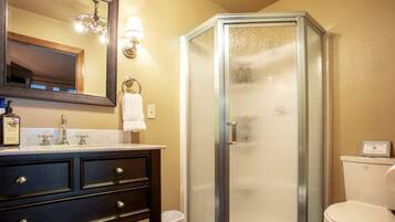 A bathroom with a dark vanity, a mirror, a glass shower enclosure, and a toilet.