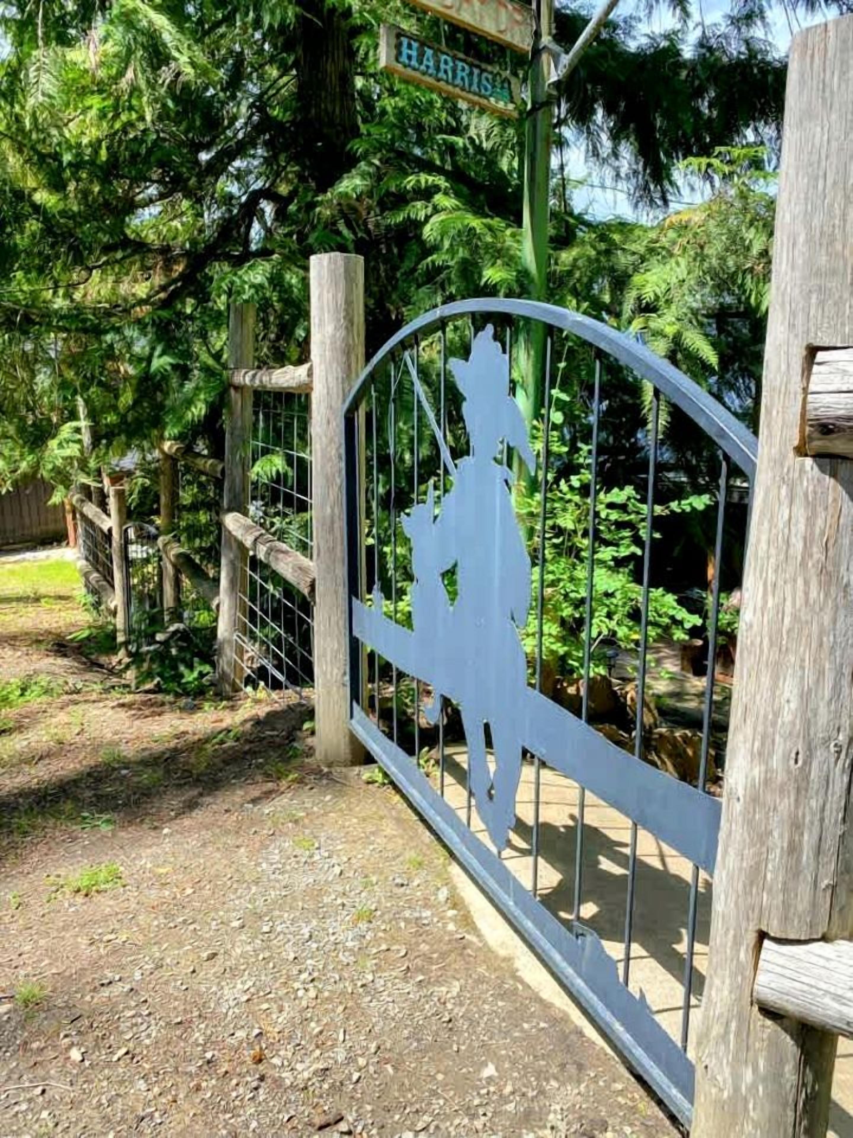 A wooden gate with a metal gate, a sign above it, and a pathway leading into a wooded area.