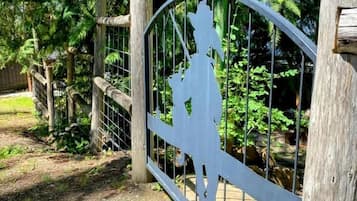 A wooden gate with a metal gate, a sign above it, and a pathway leading into a wooded area.