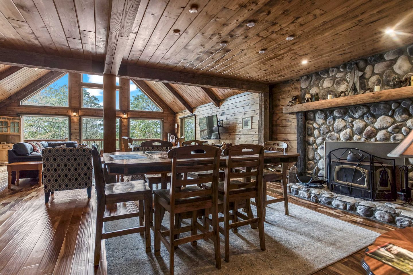 Un intérieur en bois avec une cheminée en pierre, un coin repas et de grandes fenêtres.