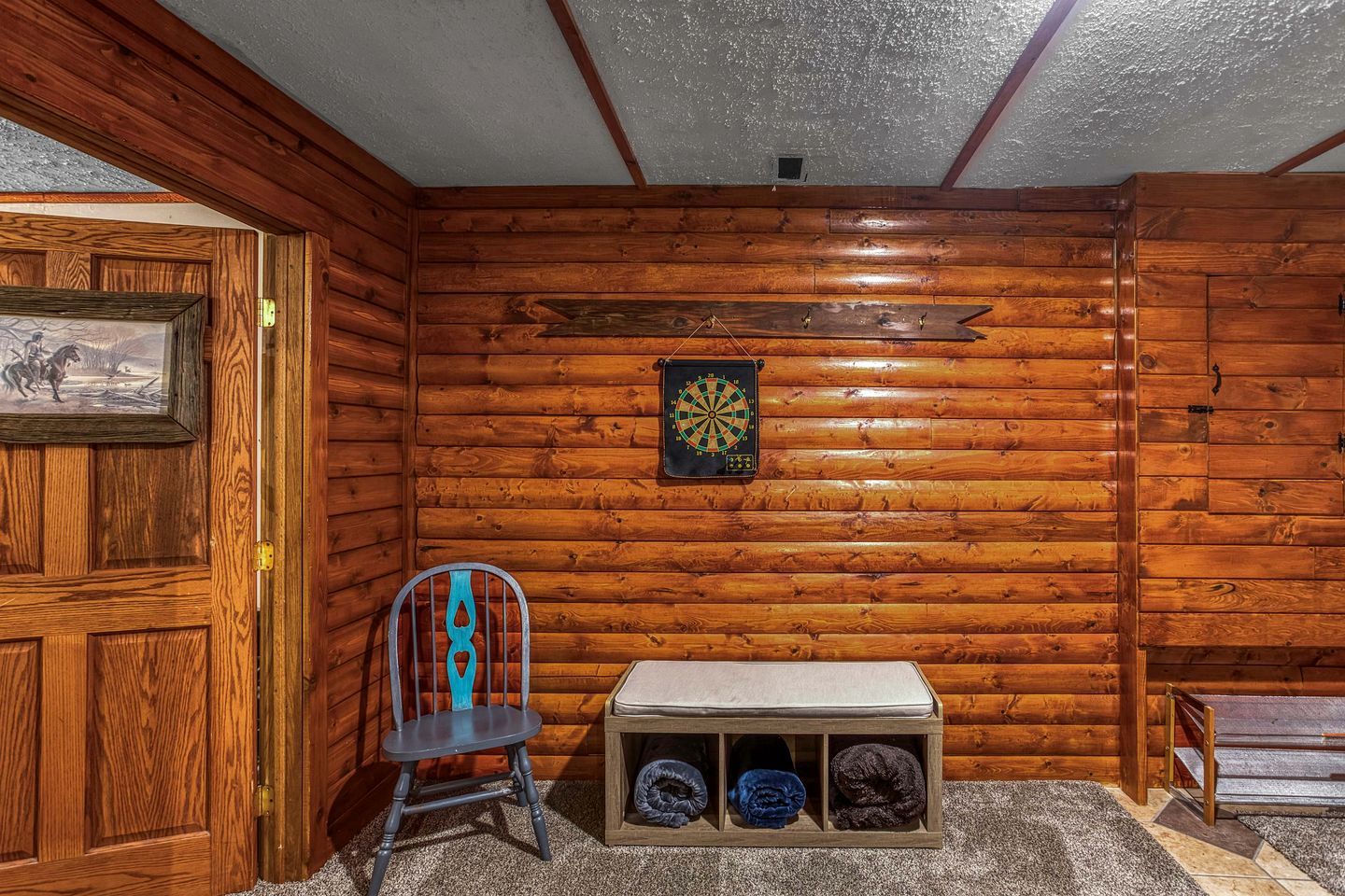 Um quarto com paredes de madeira, um alvo de dardos, uma cadeira e um banco com espaço de armazenamento.