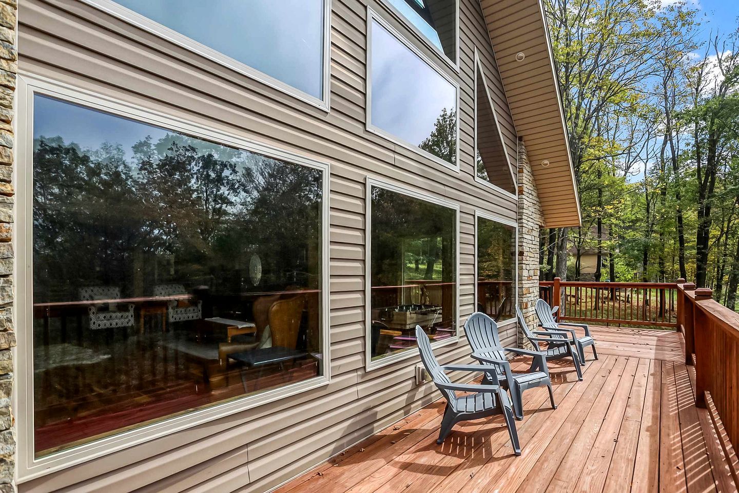 A wooden deck with outdoor seating and large windows overlooking a forested area.