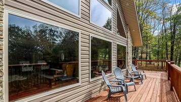 A wooden deck with outdoor seating and large windows overlooking a forested area.