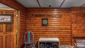 A room with wooden walls, a dartboard, a chair, and a bench with storage.