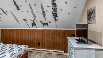 Um quarto com cama, cômoda, televisão e uma parede com um mural de tema natural.