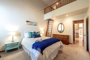 A bedroom with a bed, bedside tables, a dresser, a mirror, a staircase, and an open door leading to another room. - Enchanting Vacation Rental with Breathtaking Lake Views near Lake Fernan in Idaho (Coeur d'Alene)