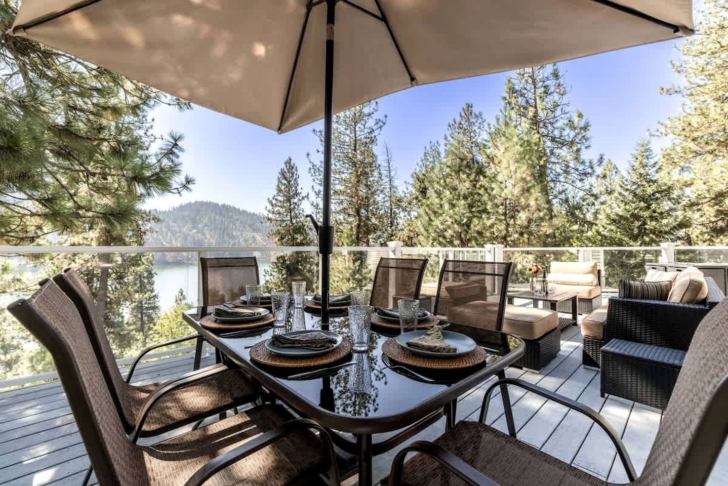 A deck with a table set for dining, overlooking a lake and forest.