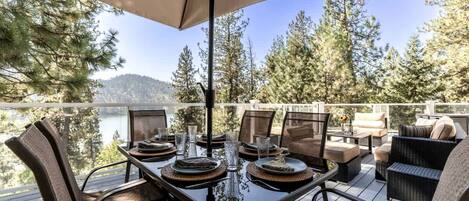A deck with a table set for dining, overlooking a lake and forest.