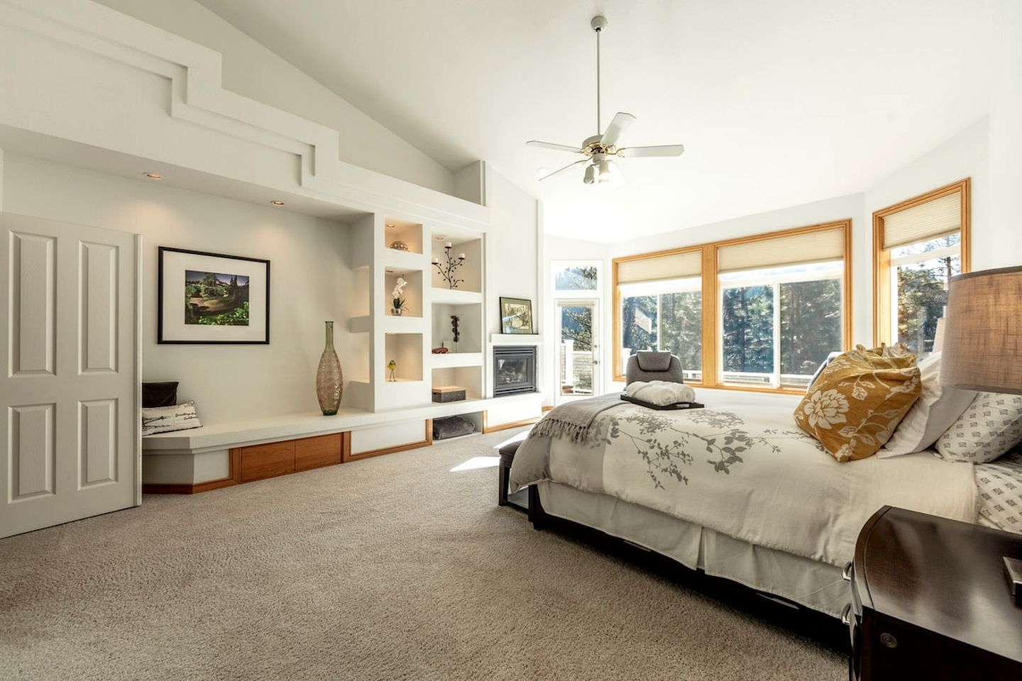 A bedroom with a bed, a seating area with a bench, a fireplace, and large windows.
