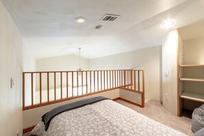 A bedroom with a sloped ceiling, a wooden railing, a bed with patterned bedding, and a built-in shelving unit. - Enchanting Vacation Rental with Breathtaking Lake Views near Lake Fernan in Idaho (Coeur d'Alene)