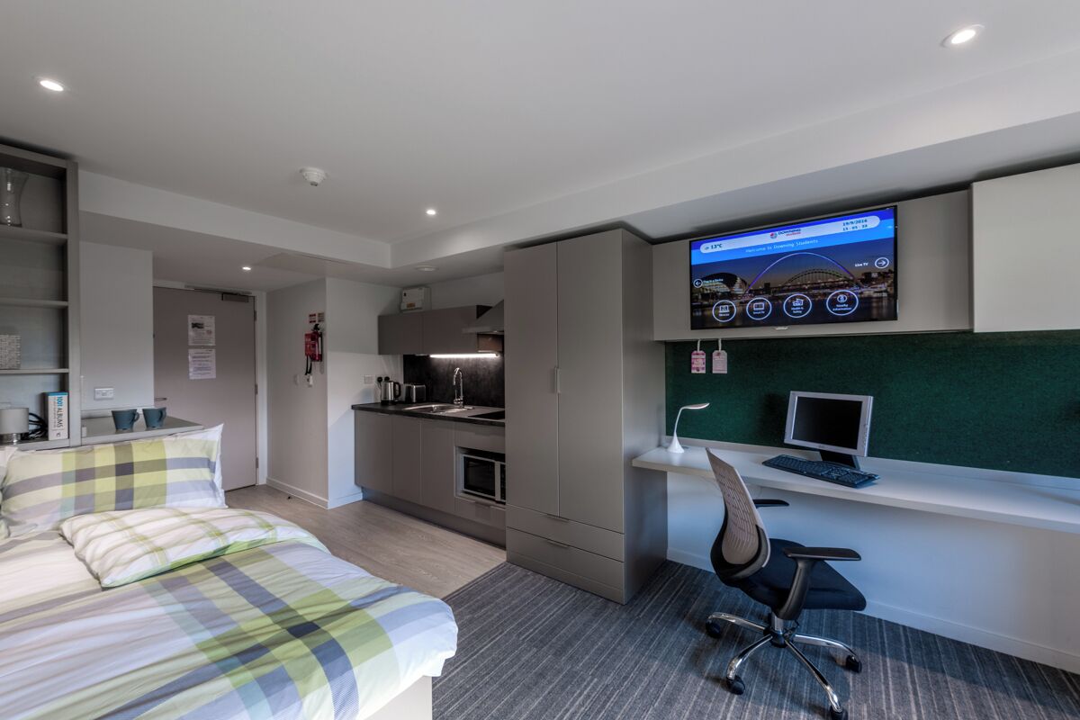 A modern hotel room with a bed, a desk, a computer, and a television.