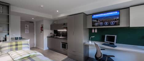 A modern hotel room with a bed, a desk, a computer, and a television.